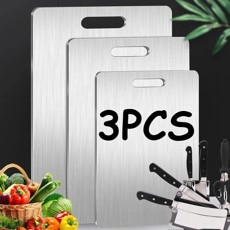 A set of three stainless steel double-sided cutting boards displayed against a dark background with fresh produce.