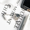 A close-up of a silver studio-grade wired in-ear monitor resting on white paper next to a smartphone.
