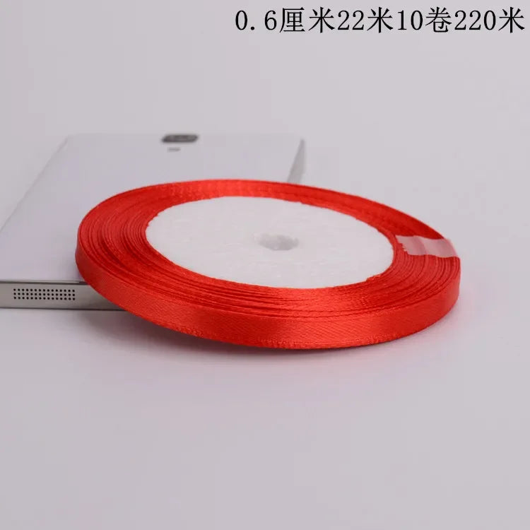 A roll of bright red satin ribbon is shown on a white surface.