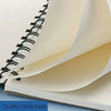 A close-up view of a spiral-bound sketchbook showing the quality inside page and thick watercolor paper.