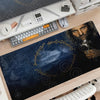 A large dark blue gaming mouse pad featuring Lord of the Rings imagery and a keyboard setup on a wooden desk.