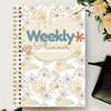 A spiral notebook titled Weekly Planner featuring a floral pattern with light blue and beige accents.