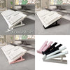 A set of white and pink keyboard risers used to elevate a computer keyboard for ergonomic typing.
