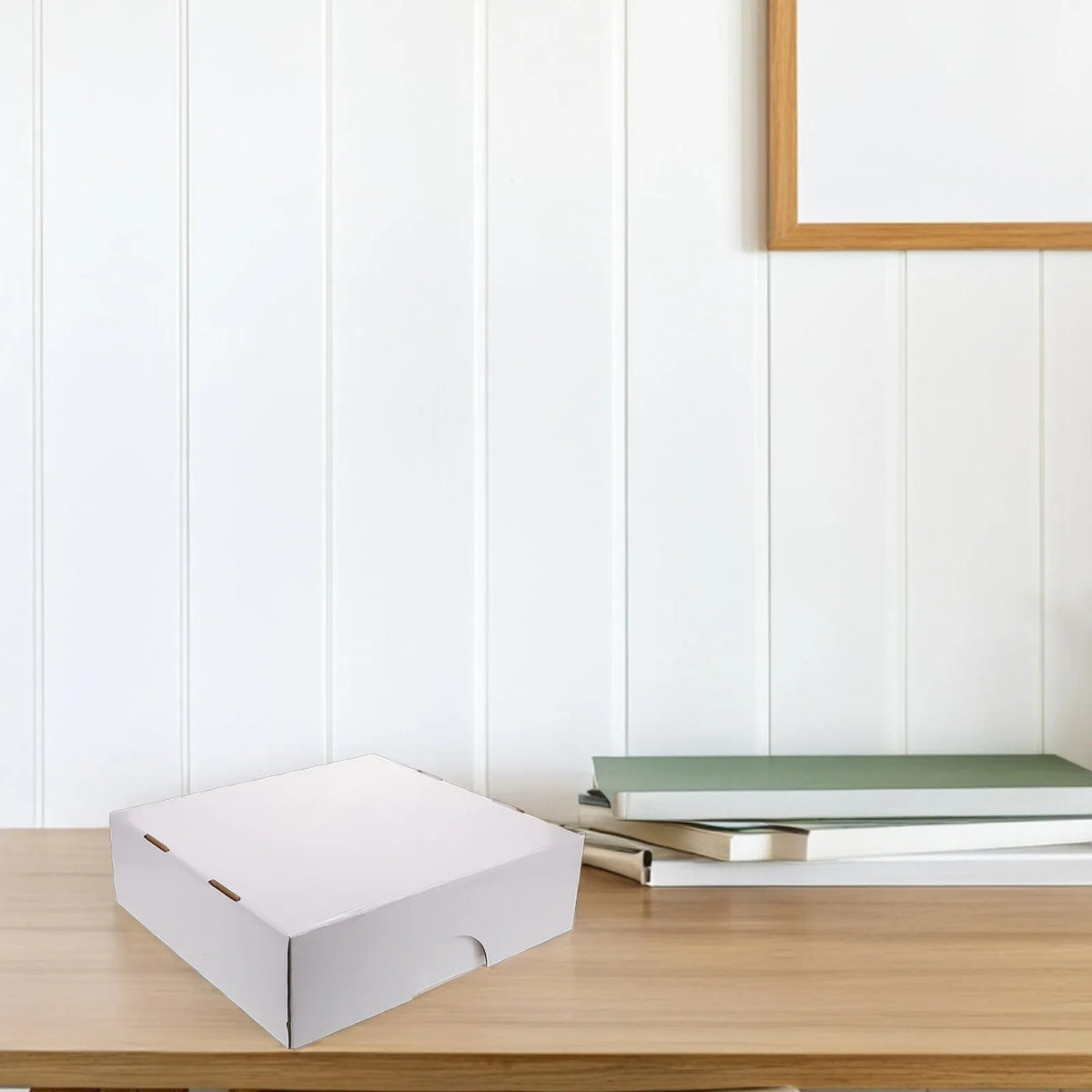 Una caja rectangular blanca de almacenamiento para cartas coleccionables sobre una mesa de madera junto a libros apilados.