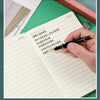 A hand writes in a lined page of a premium A5 leather journal with a black pen on a green surface.
