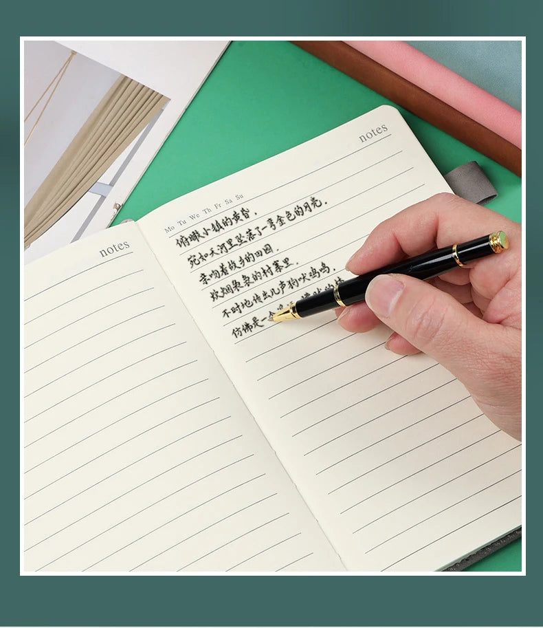 A hand writes in a lined page of a premium A5 leather journal with a black pen on a green surface.