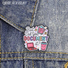 An enamel pin featuring the text But Did You Document It? with a pink laptop and a cup on a denim fabric background.