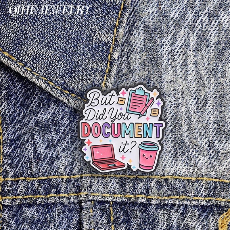 An enamel pin featuring the text But Did You Document It? with a pink laptop and a cup on a denim fabric background.