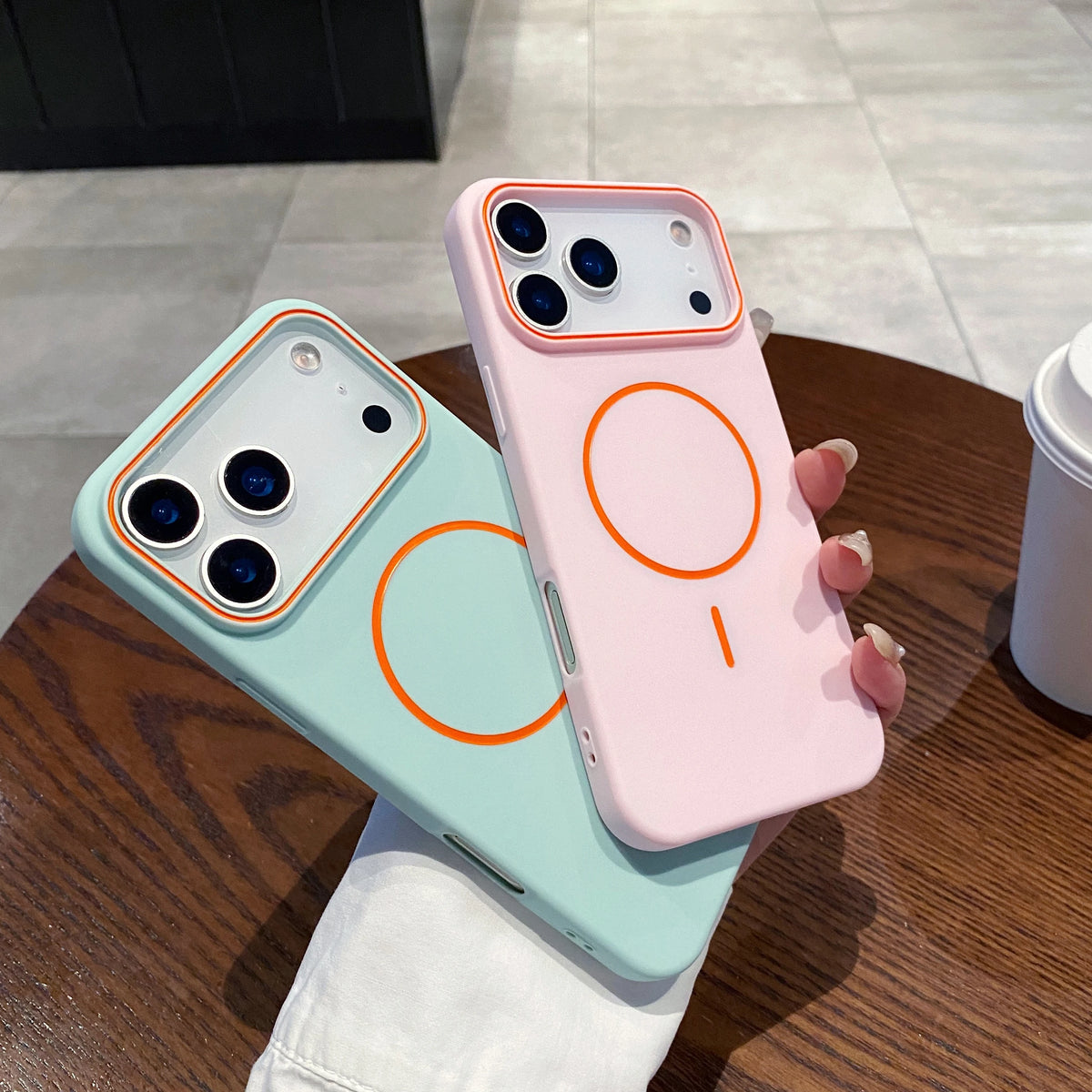 A pink phone case with an orange circular design is displayed next to a light blue version on a wooden table.