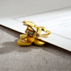A close-up of a gold-colored, iris-shaped metal binder clip with a spring mechanism resting on a white card against a gray su