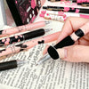 A hand holds a set of six pink and black butterfly design gel pens on a white surface.