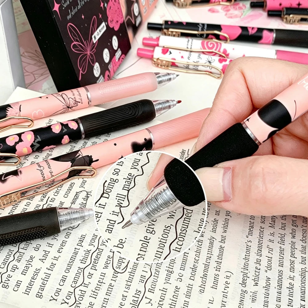 A hand holds a set of six pink and black butterfly design gel pens on a white surface.