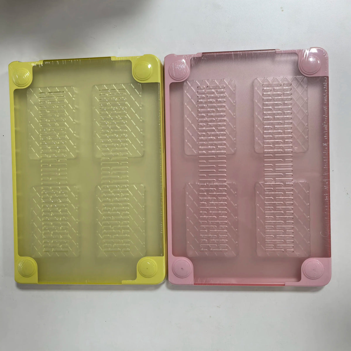 Two translucent hard shell laptop cases, one yellow and one pink, showing textured internal inserts.