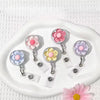 A clear retractable ID badge holder with a floral pull buckle resting on a white tray.