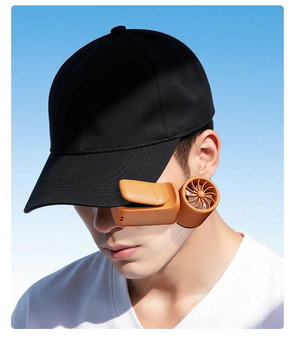 A close-up of a person wearing a black baseball cap and an orange portable rechargeable handheld cooling fan.