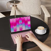 A person is typing on a laptop with a pink silicone keyboard cover on a dark table.