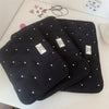 Black padded laptop sleeve case with white stud detailing lying on a white surface.