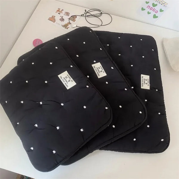Black padded laptop sleeve case with white stud detailing lying on a white surface.