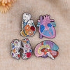 A set of enamel pins featuring medical themes including a heart, lungs, and brain.