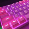 Close-up of a pink backlit mechanical keyboard keycaps showing letters and function keys.