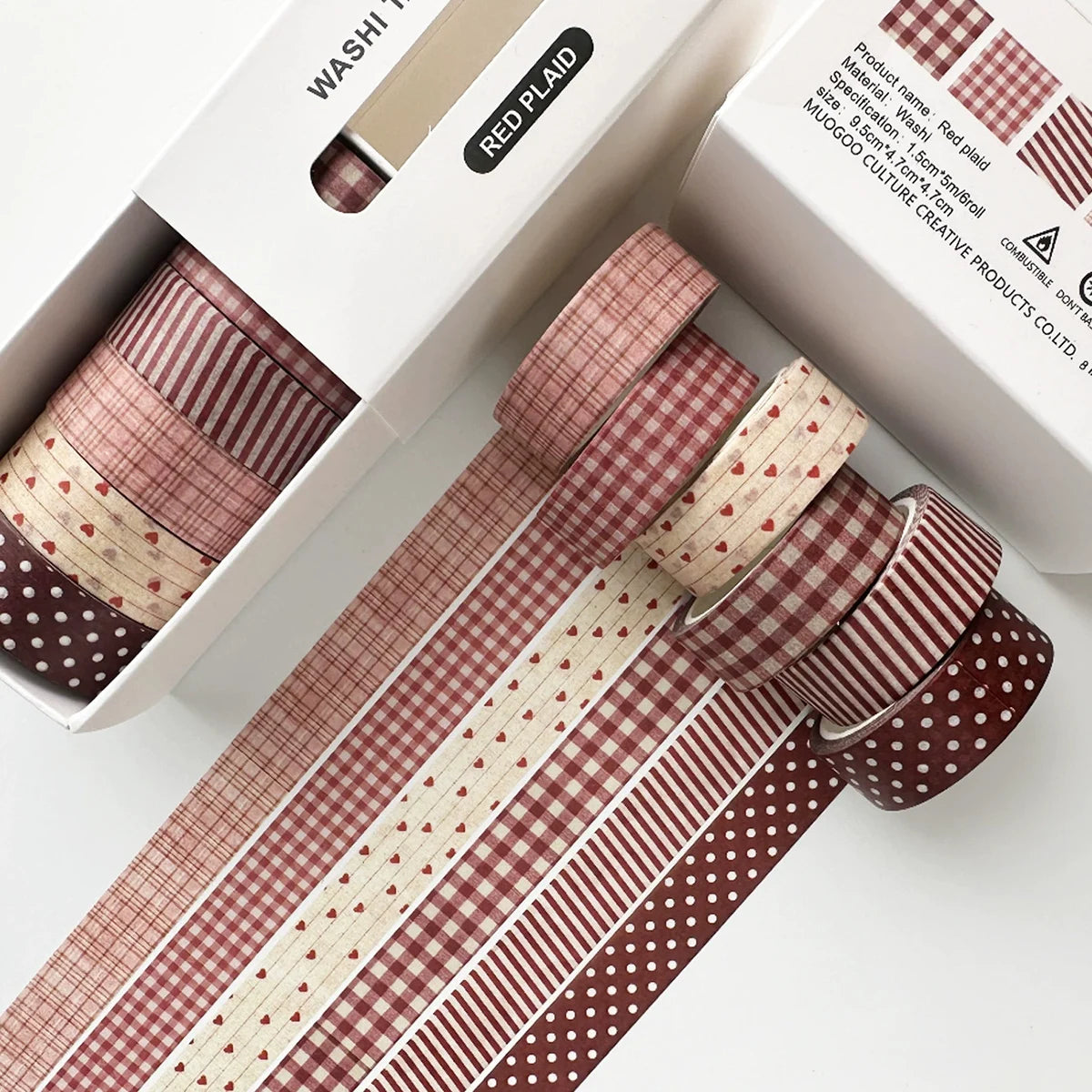 A set of red plaid and polka dot washi tape rolls displayed in a box for crafting and journaling.