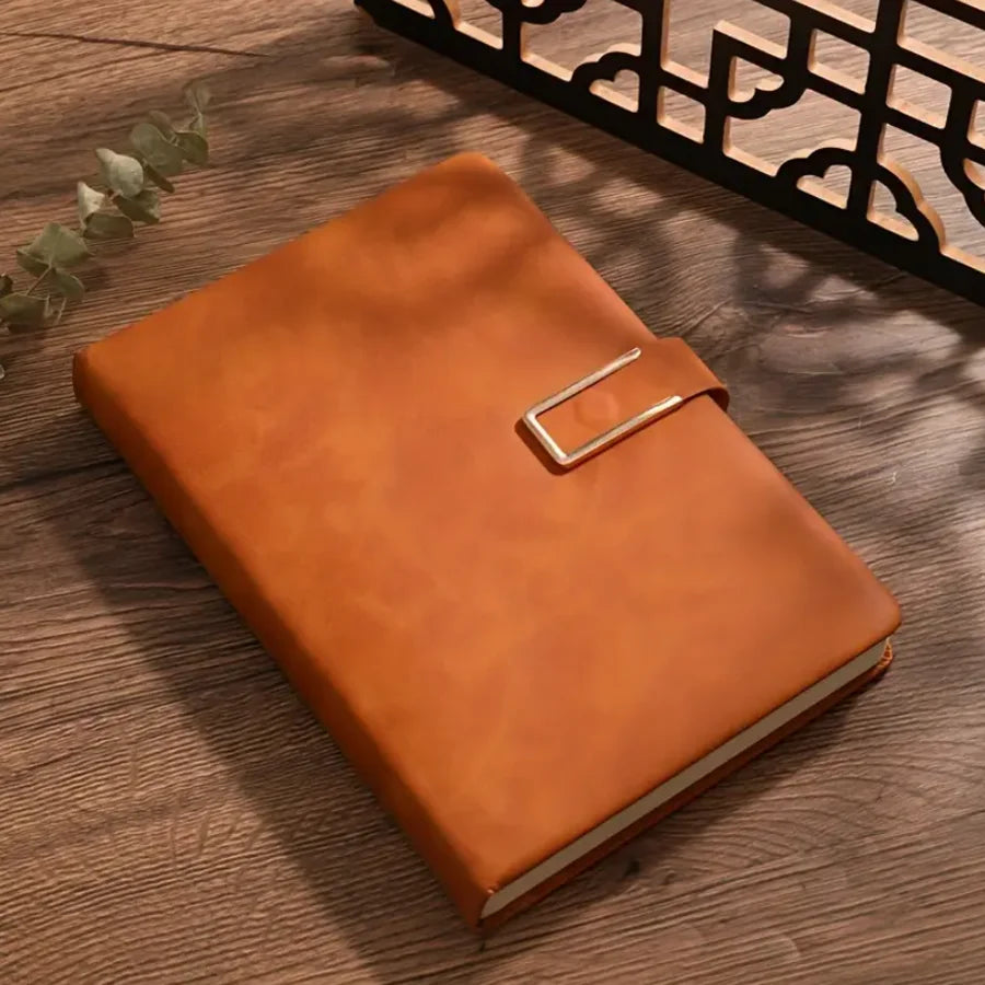 A brown leather notebook with a silver clasp is placed on a wooden surface next to an ornate black metal shelf.