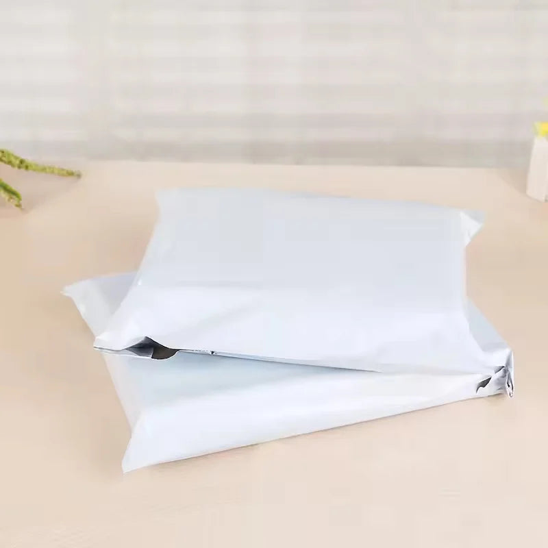 A stack of white self-sealing plastic mailing bags lying on a light surface.