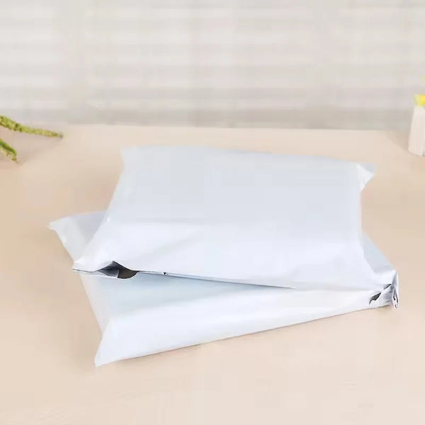 A stack of white self-sealing plastic mailing bags lying on a light surface.