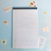 A white lined writing pad is shown with a fruit sticker and a small yellow coin nearby.