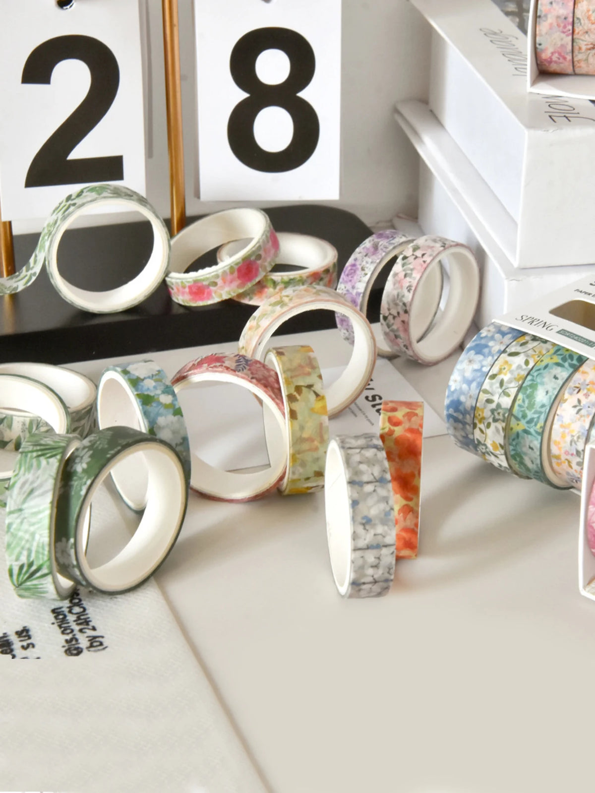 A collection of five rolls of floral patterned washi tape in various colors and designs displayed on a white surface.