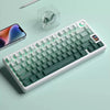 Vista cercana de un teclado mecánico blanco con teclas verdes e iluminación RGB sobre una superficie azul claro.