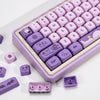 A close-up view of a purple Magic Bunny PBT keycap set with various function keys and modifiers arranged in a plastic case.
