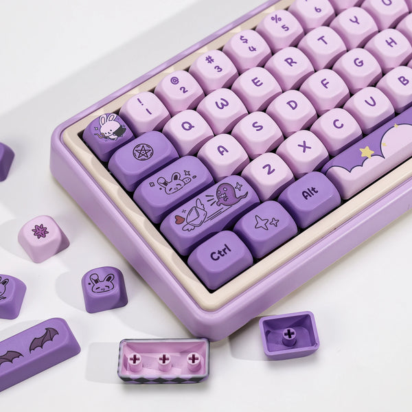 A close-up view of a purple Magic Bunny PBT keycap set with various function keys and modifiers arranged in a plastic case.