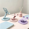 A set of three pastel colored foldable desktop phone stands with wooden sticks, displayed on a light pink table.