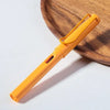 An orange fountain pen is resting on a wooden board.