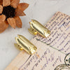 A set of gold metal beetle binder clips resting on aged paper next to a dried flower.