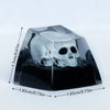 A clear resin skull model resting on a black base, shown at an angle with measurement lines.