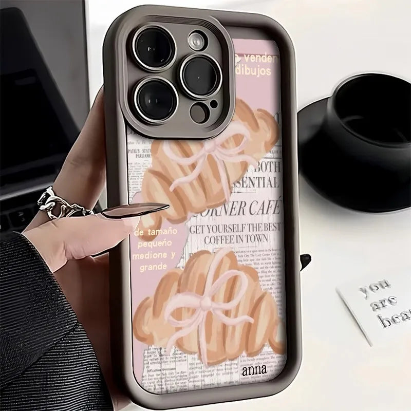 A phone case featuring a croissant newspaper pattern with a floral ribbon design.