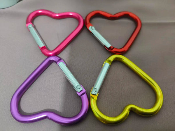 A collection of five colorful heart-shaped spring clasps and carabiner keychains in pink, red, purple, and yellow.