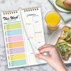 A hand holds an open weekly meal planner and grocery list pad with organized meal plans and shopping lists.