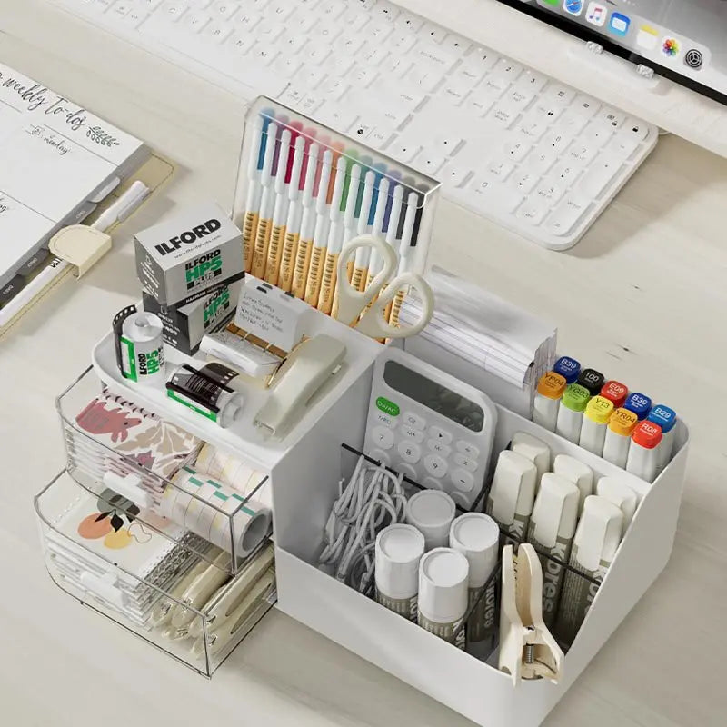 A white desk organizer with clear storage drawers holds various pens, pencils, and office supplies.