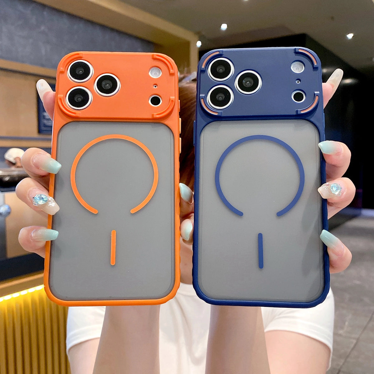 Two frosted magnetic silicone cases for an iPhone, one orange and one blue, held by a person.