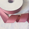 A roll of matte finish satin ribbon in dusty rose pink is shown next to a long, rolled-up strip.