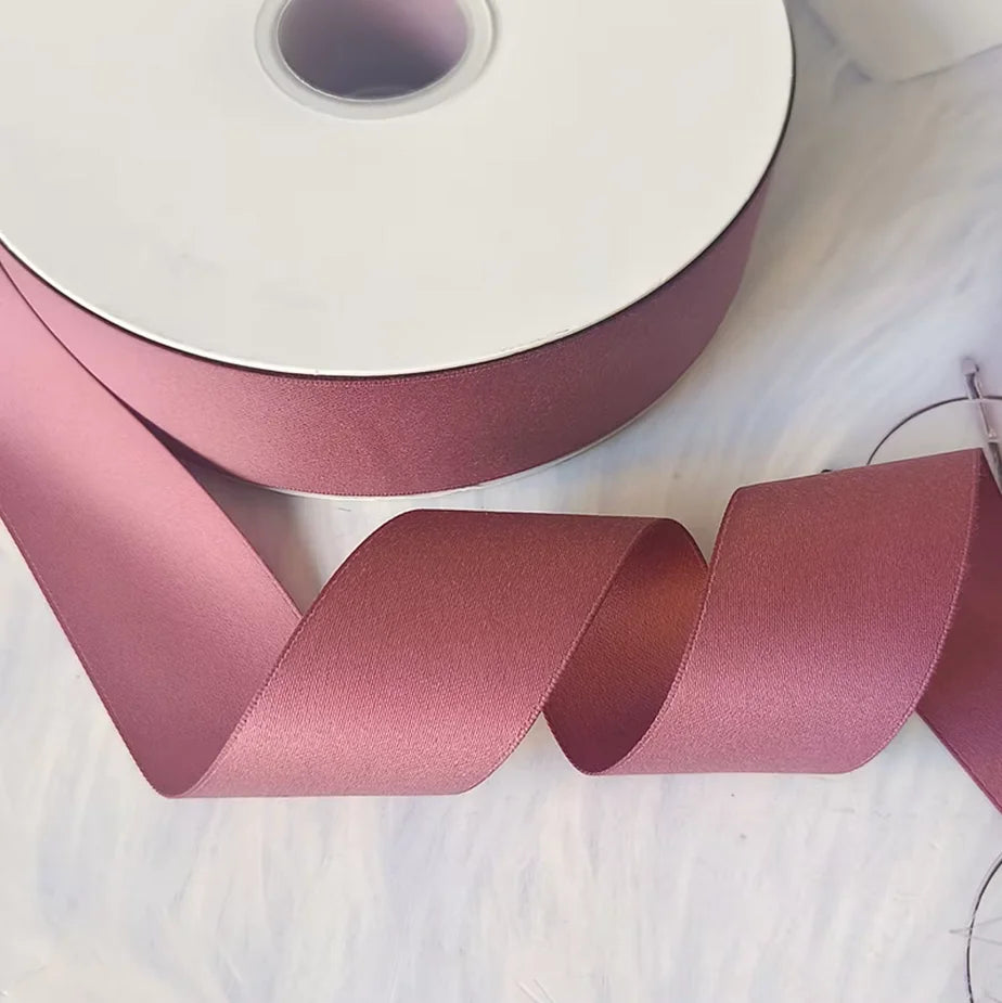 A roll of matte finish satin ribbon in dusty rose pink is shown next to a long, rolled-up strip.