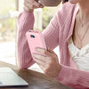 A person holds a pink power bank with a built-in AC plug and dual cables while sitting at a wooden table.