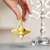 A hand is holding a gold-colored metal spinning top fidget toy above a gray surface.
