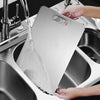 A hand is placing a stainless steel cutting board into a kitchen sink, showing the double-sided design.