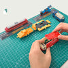 A hand places a red and black component onto a green cutting mat with grid guides, showing a model kit assembly.