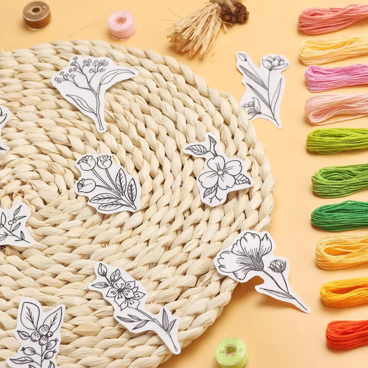 A collection of white floral embroidery patterns printed on water-soluble paper alongside various colored embroidery floss.