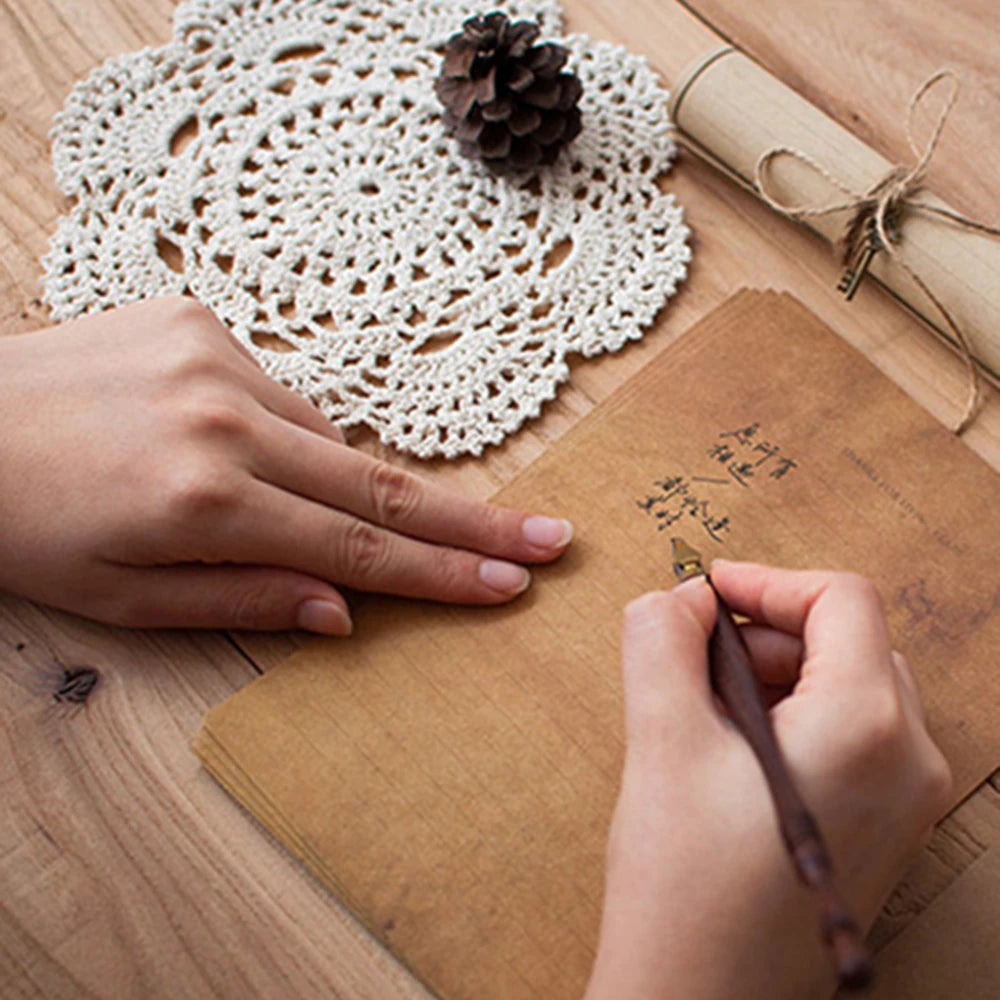 A hand is writing on a kraft paper envelope with a pen, next to a macrame coaster and a rolled parchment.